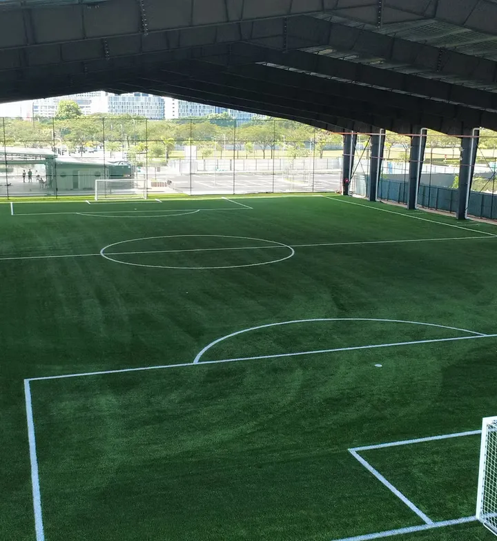 The covered 7-a-side and 9-a-side pitch at Batu Kawan seen from under its roof, marked out on FIFA-quality turf behind perimeter netting