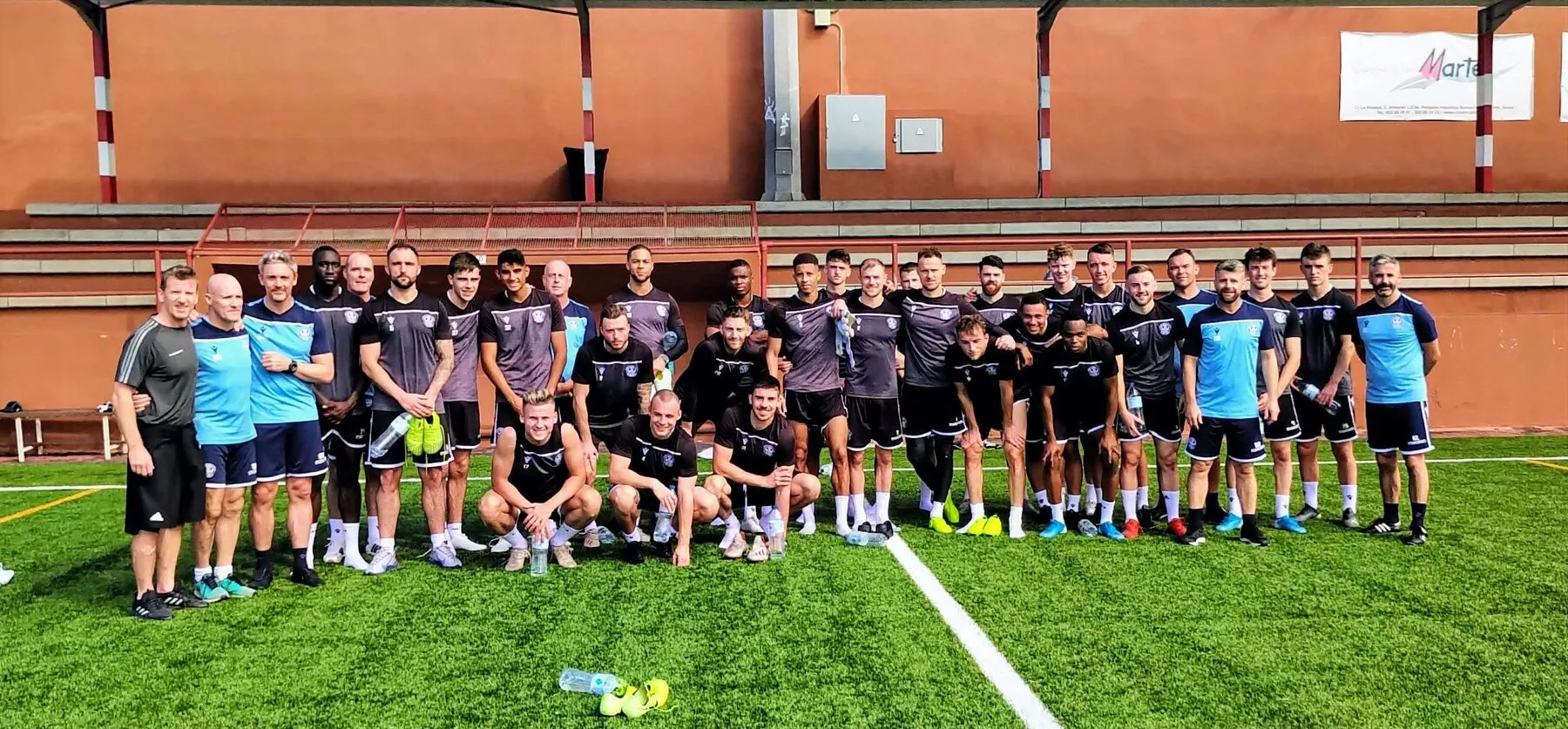 Two squads lined up on a training pitch in front of a brick stand during a Soccer Experience winter camp in Spain