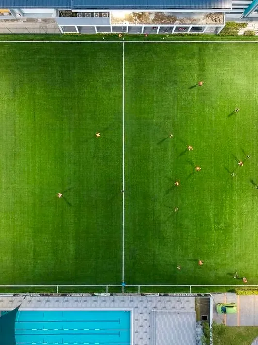 The Tanjung Bungah 9-a-side pitch seen straight down from above with a session in progress, the clubhouse at one end and the pool at the other